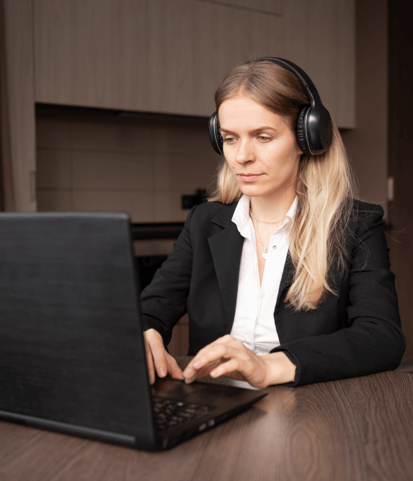 A professional woman wearing headphones working on the laptop for the precise and accurate automated transcription services.