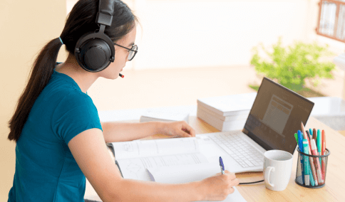 Side view of a woman working on a laptop at a table, representing fast, affordable, and flexible transcription services.