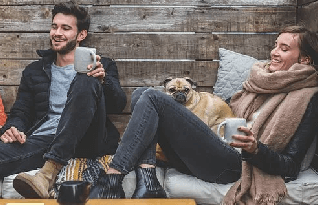  Man and woman on a wooden bench holding with their pet dogcoffee mugs