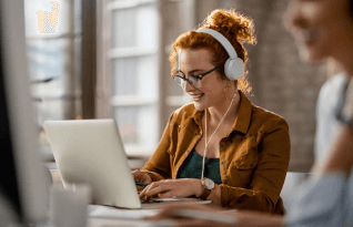   Smiling creative businesswoman listening music on headphones while working on a computer in the office