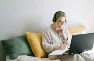 Transcriber with headphones with an open laptop taking notes