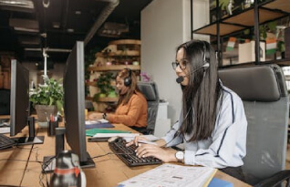 Two women trping into their desktops with headphones on